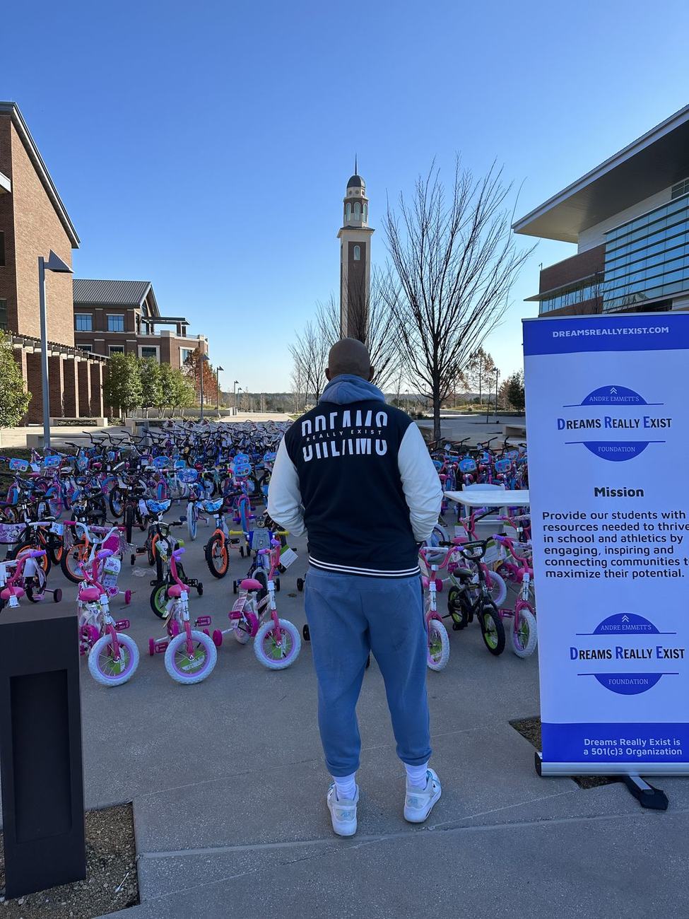 A Dreams Really Exist team member at the branded banner overlooking rows of bikes ready for children